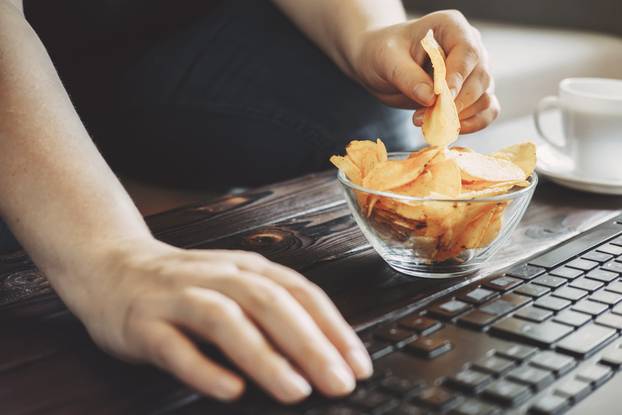 Woman eating chips from bowl at her workplace