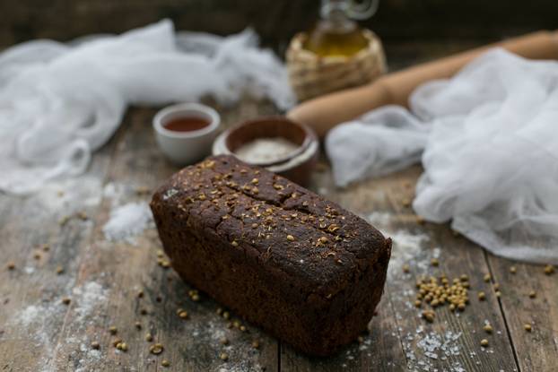 Close up view of fresh brown crispy loaf of bread lying on the wooden table sprinkled with flour.